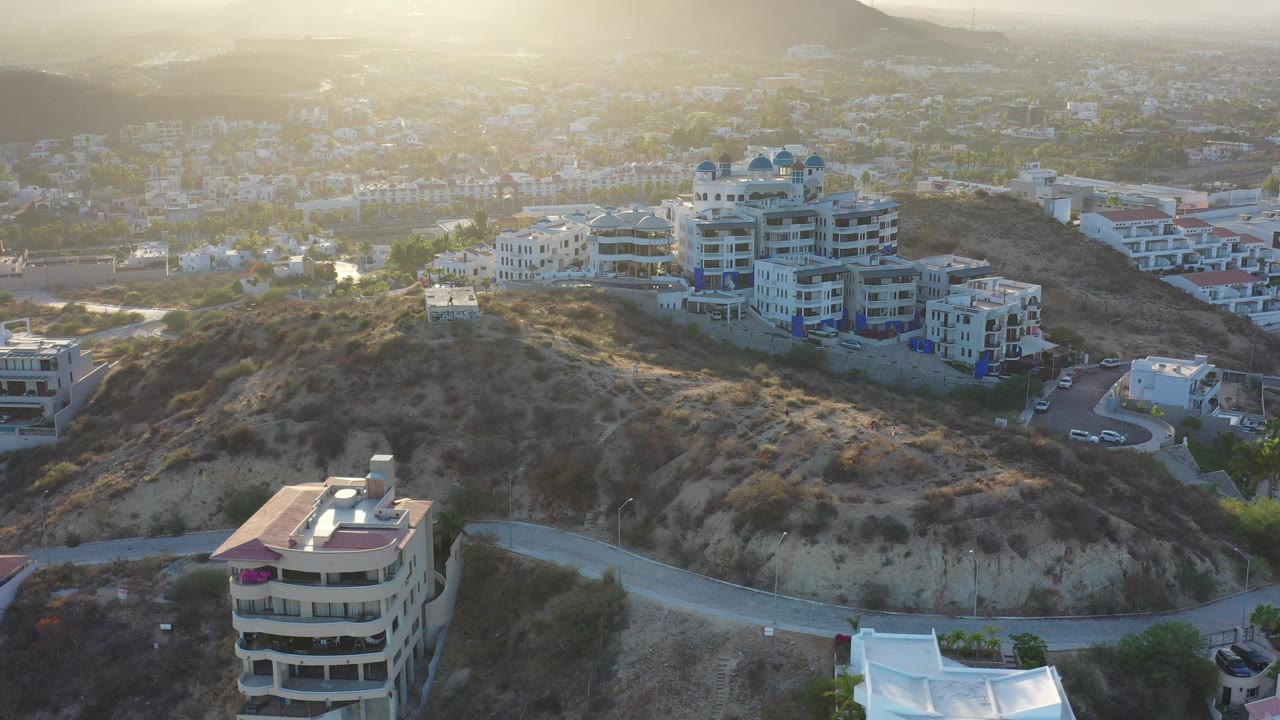 Aerial view of hillside homes and a winding road in hazy light.