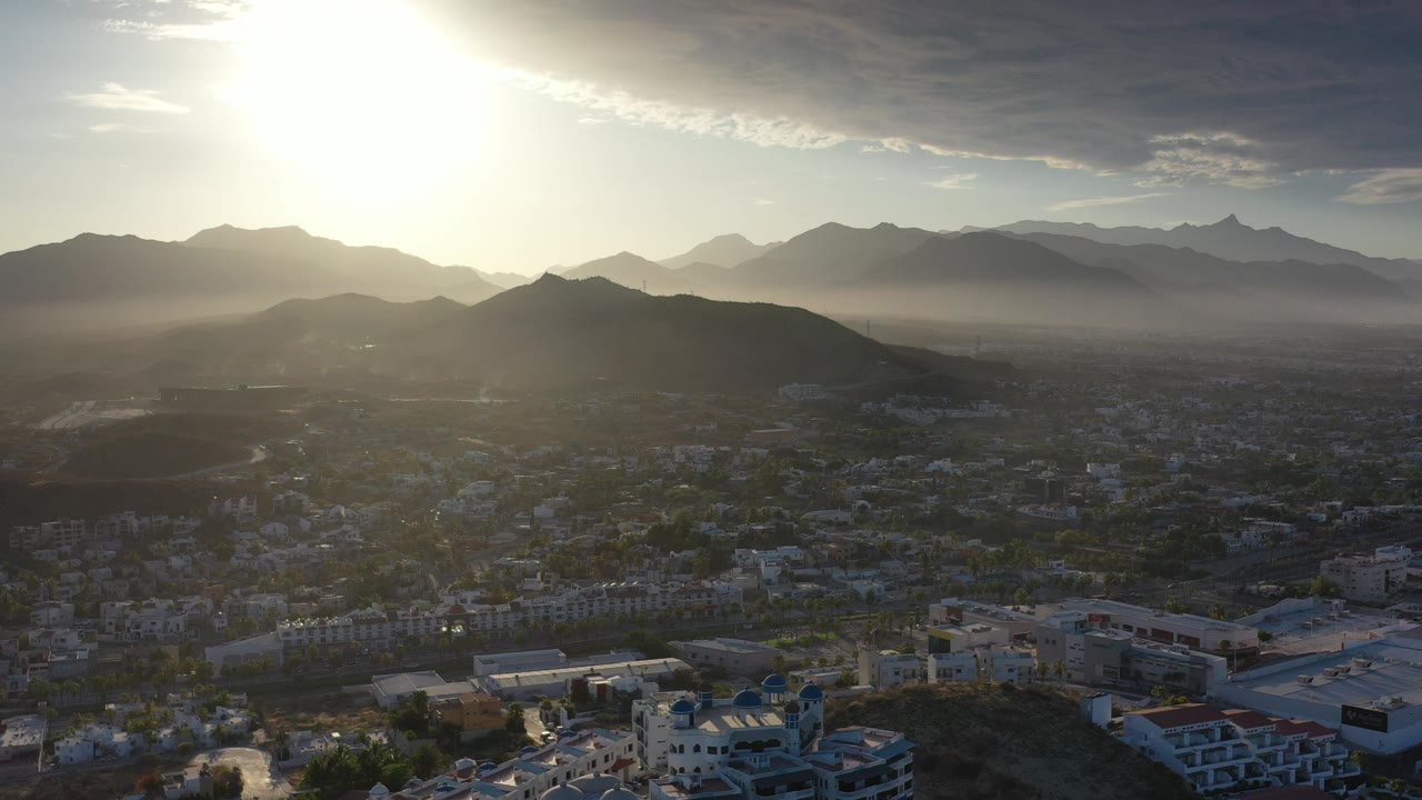 Aerial city view below sunlit mountains and haze
