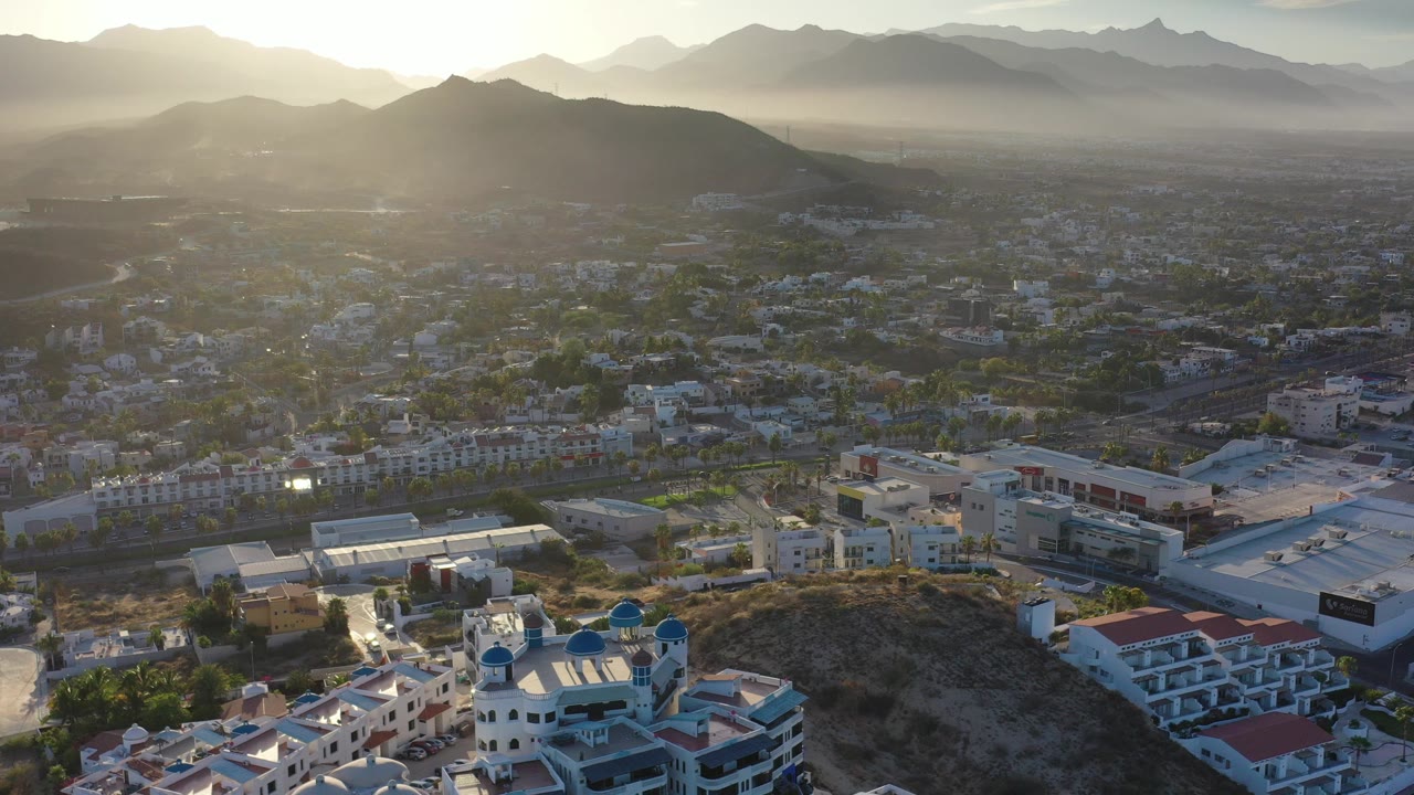 Aerial view over Los Cabos buildings with hills and mountains in haze.