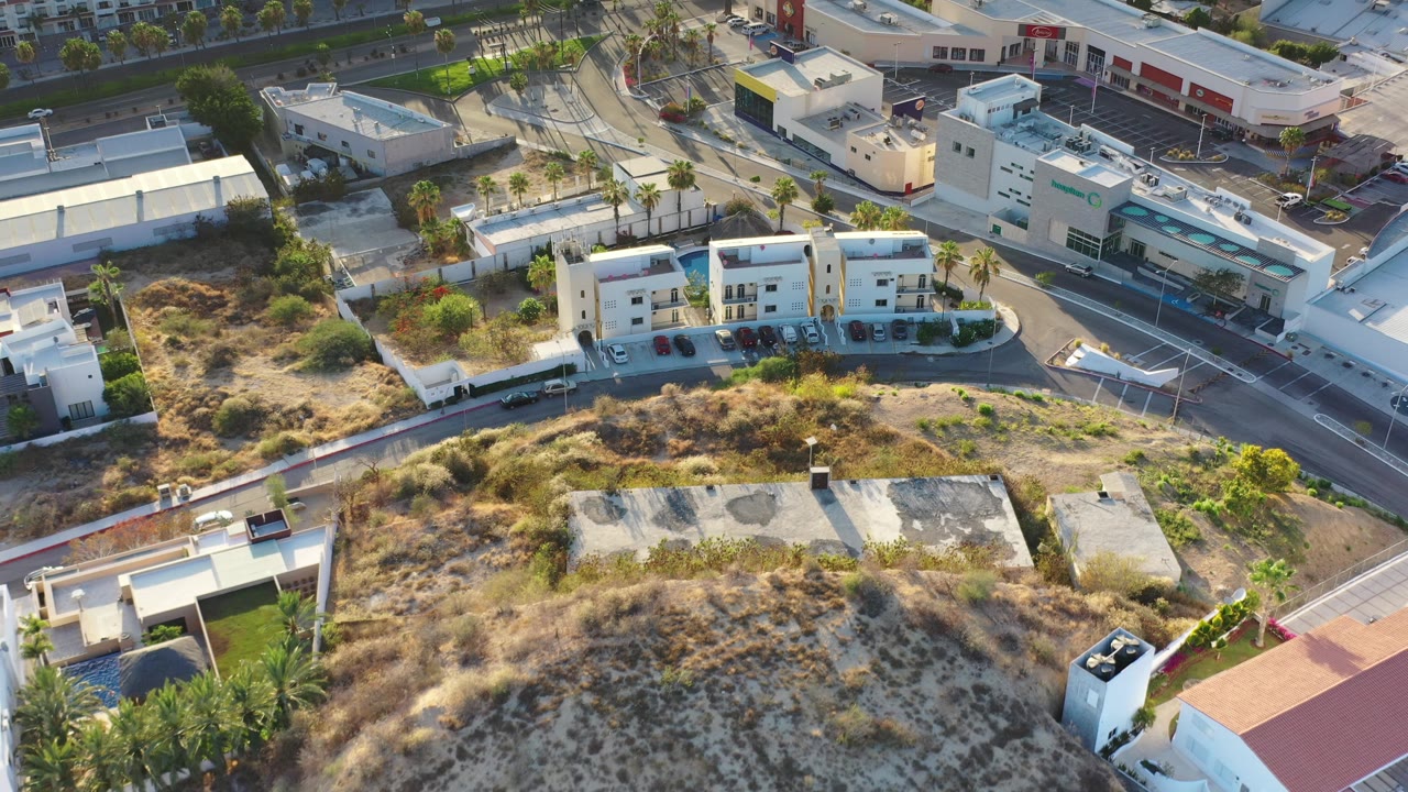 Aerial frame of white buildings, a road intersection, rooftops, and dry terrain.