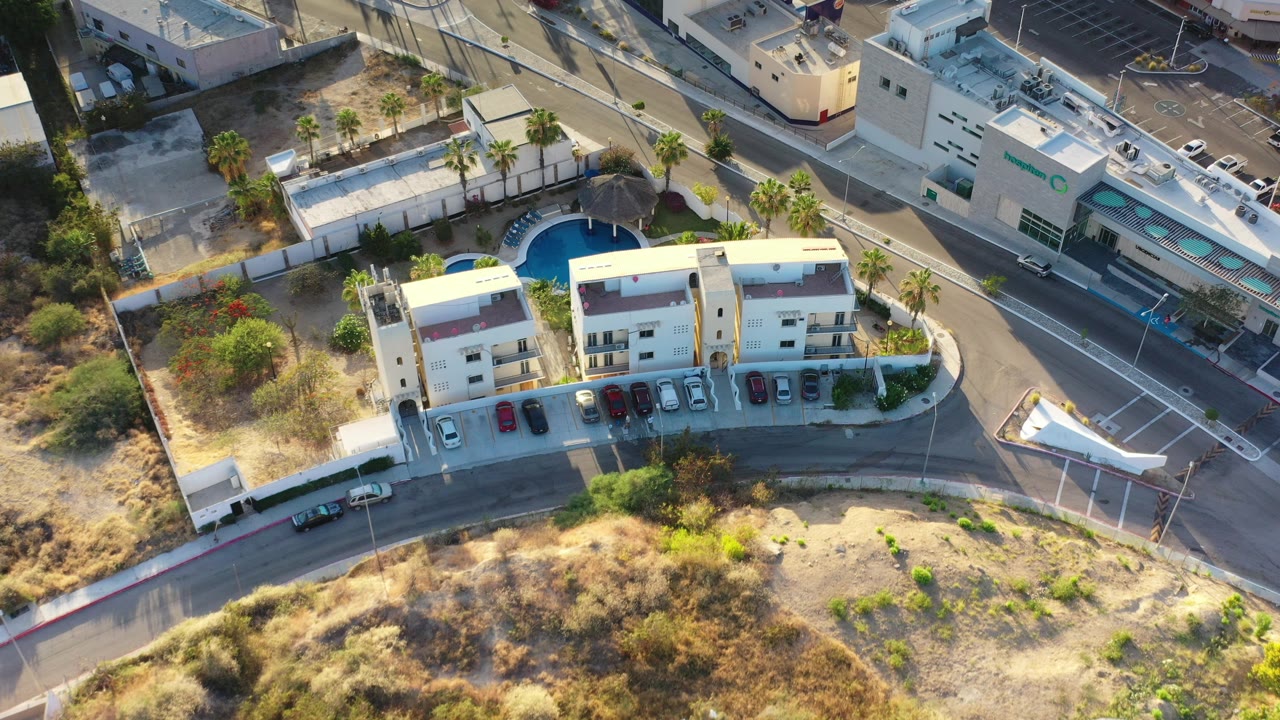 Aerial view of apartment buildings, pool area, road, parked cars, and dry lots.