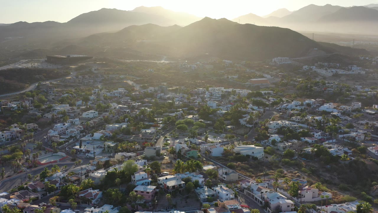 Aerial view of a hillside town below sunlit mountains.