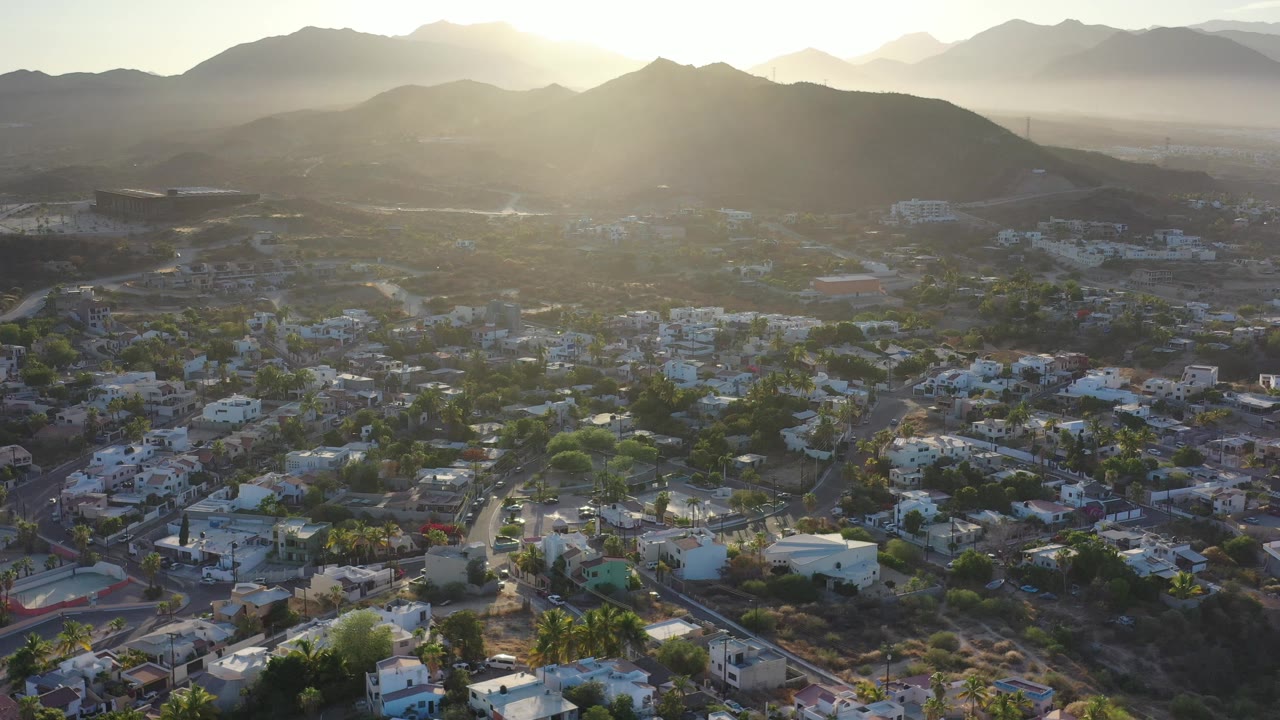 Low-rise buildings and greenery below a sunlit mountain skyline.