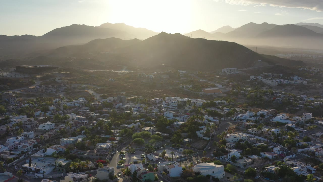 Aerial view of a town below dark mountains and bright sun.