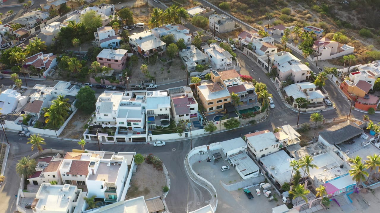 Aerial view of white houses, curved streets, palms, and dry lots.