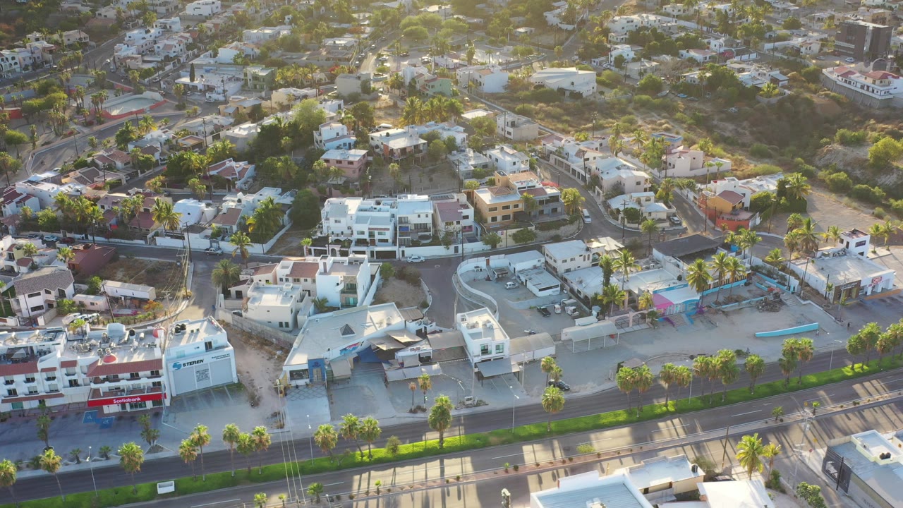 Aerial view of condos, palm-lined road, and hillside homes.