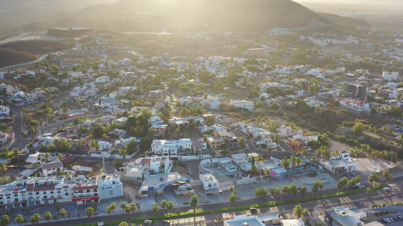 Aerial view of city buildings below sunlit mountains.