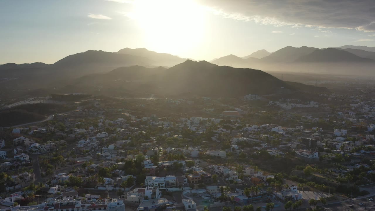 Backlit mountains and city blocks under a bright sunset.