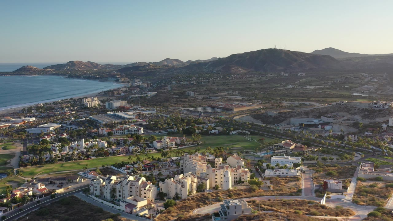 Wide aerial view of coast, town buildings, roads, and mountains.