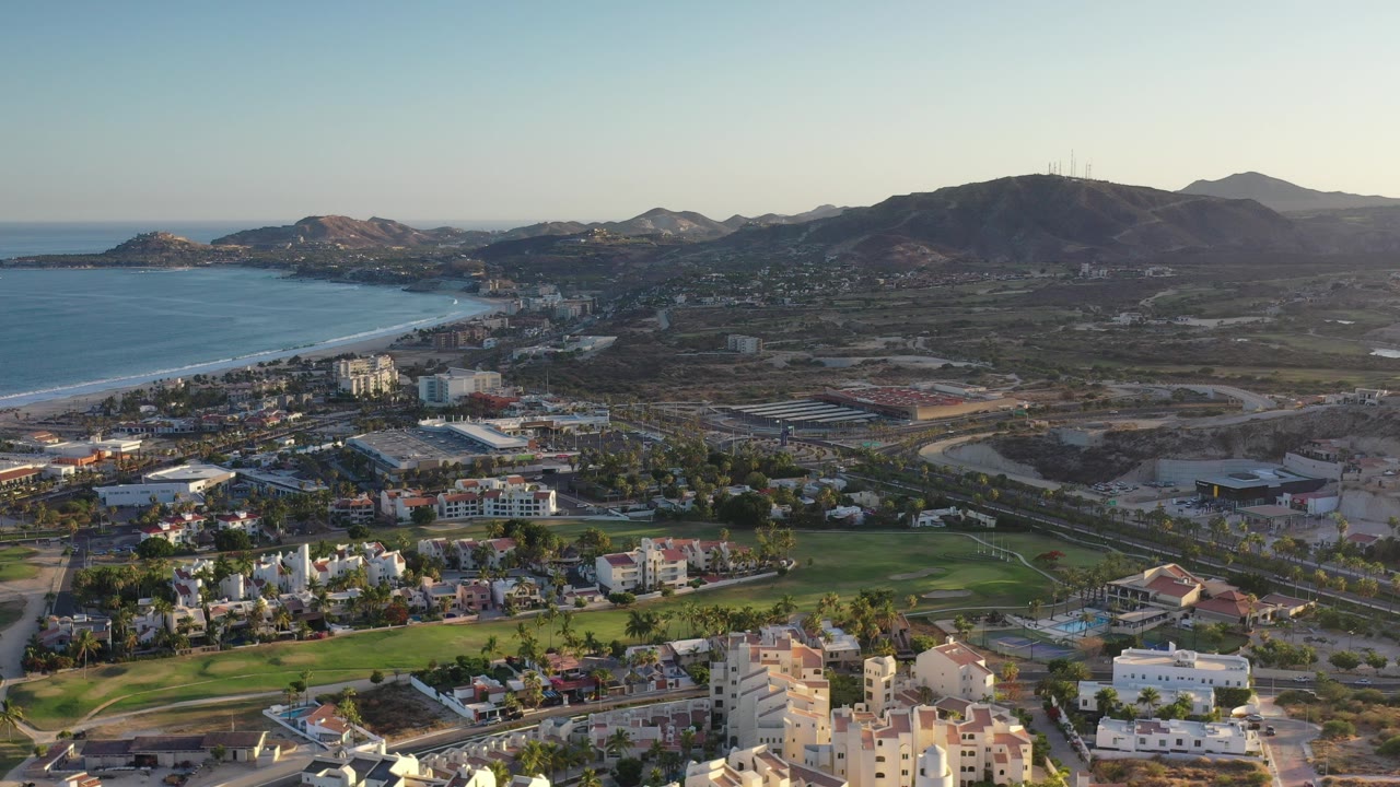 High aerial view of Los Cabos coastline, buildings, green lawns, and mountains.