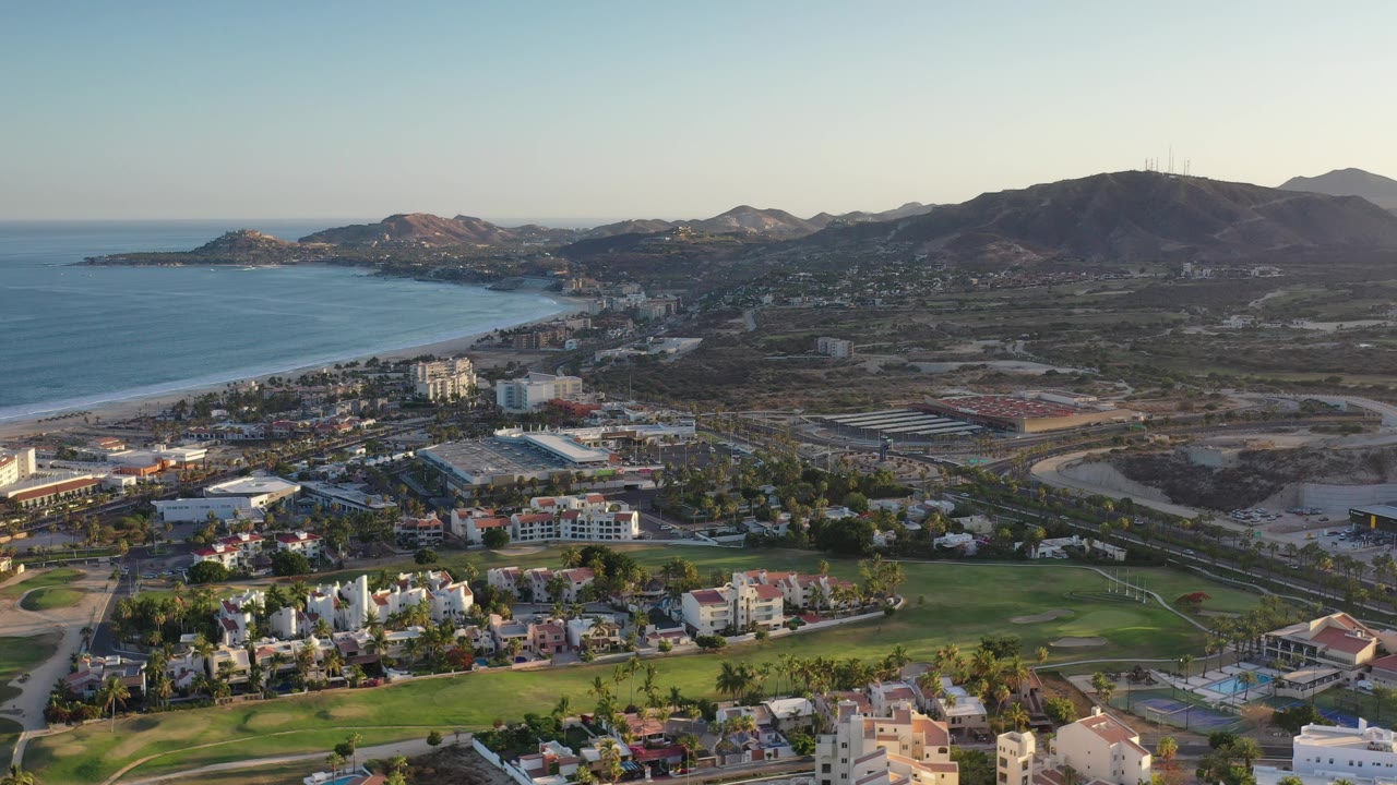 Drone-height view of beach, buildings, roads, and arid hills.