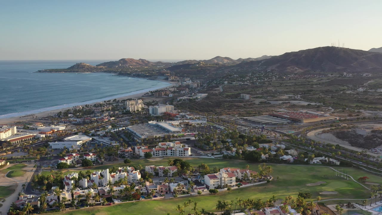 Drone-style view of beachside city, golf course, roads, and hills.