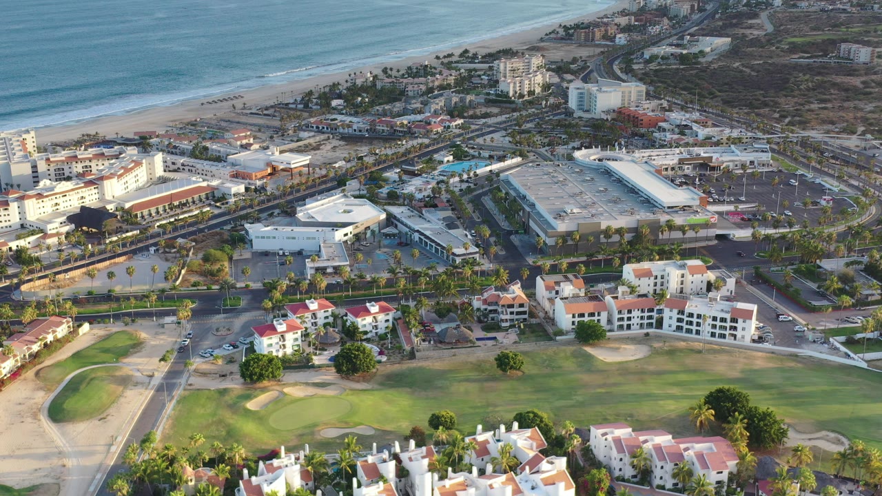 Aerial view of ocean, beach, roads, buildings, and a golf course.