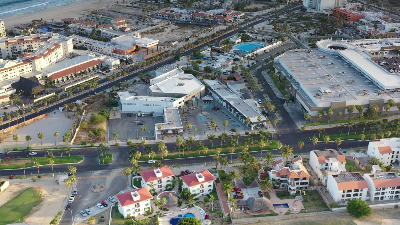 Aerial view of palm-lined street, buildings, pools, and coastline.