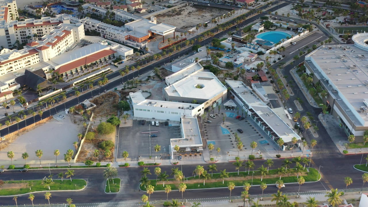 Aerial view of low-rise buildings, roads, palms, and parking areas.