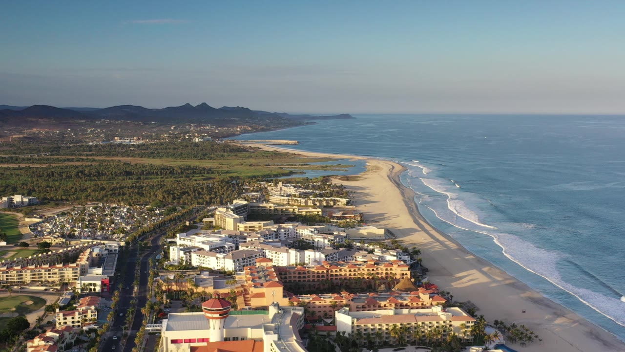 High aerial of coastal neighborhood beside a long beach and blue water.