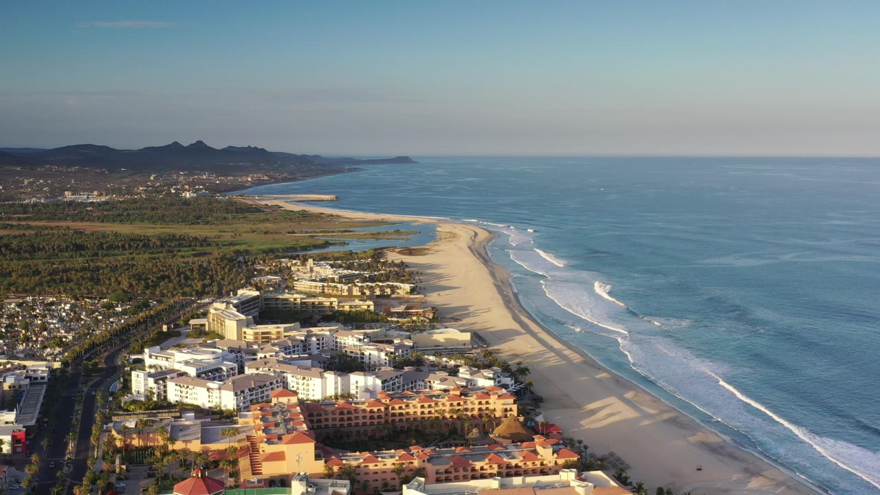 Aerial view of beach, ocean, shoreline buildings, and distant mountains.
