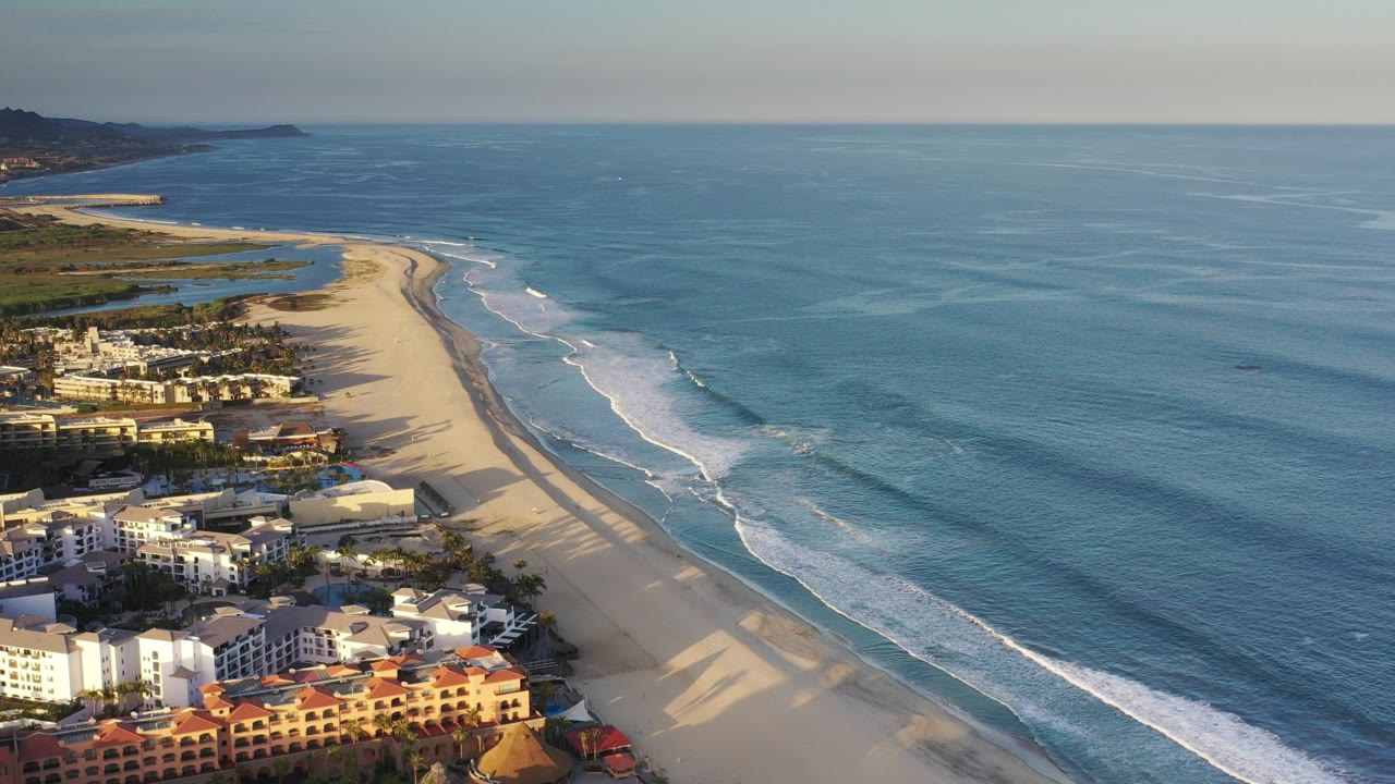 Aerial view of beachfront condos, wide sand, and blue ocean waves.