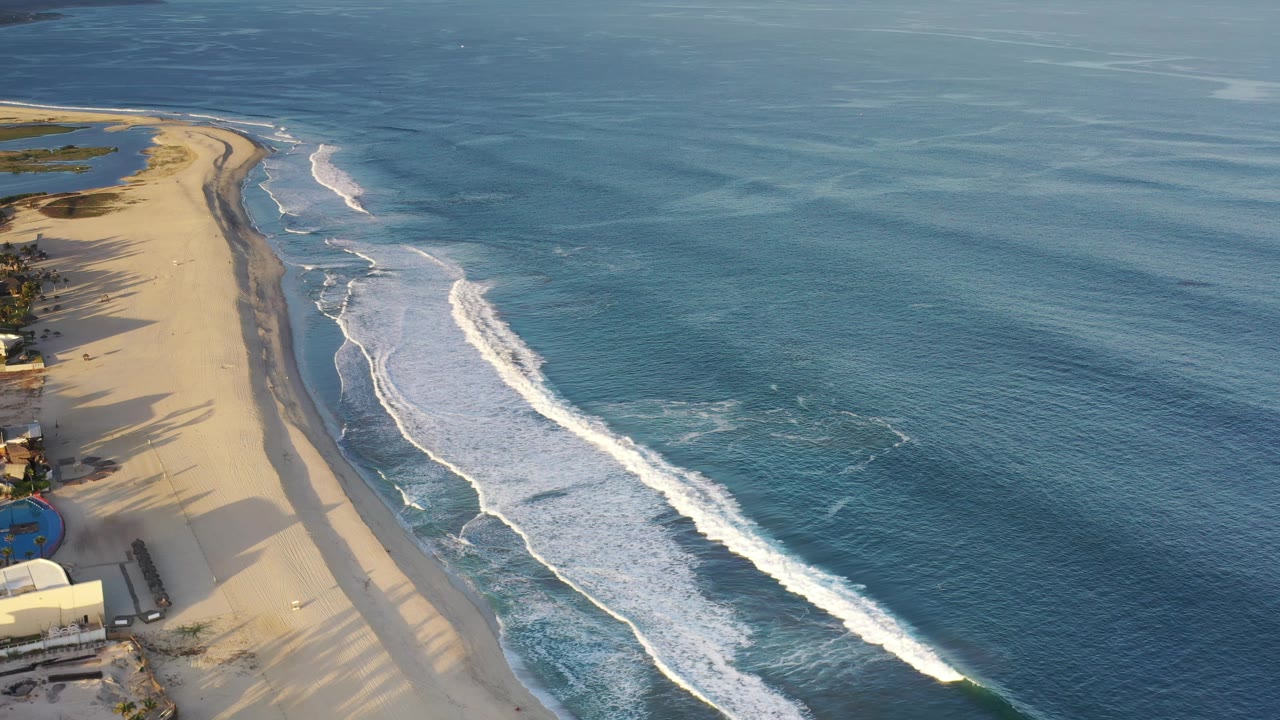 High aerial frame of Los Cabos beach with the surf line slightly farther down the coast, warm shadows on sand, and no visible people.