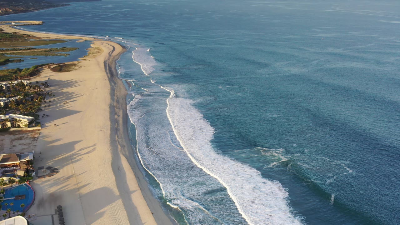 Aerial view of beach homes beside a long sandy shoreline and blue ocean surf.