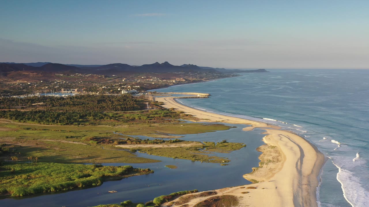 Aerial beach and lagoon with waves on the right and mountains beyond the city.