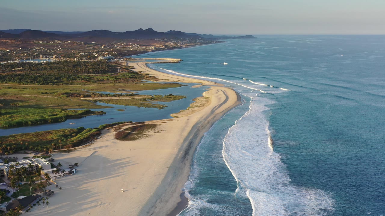 Aerial beach view with surf bands, blue water, lagoon, and mountains.