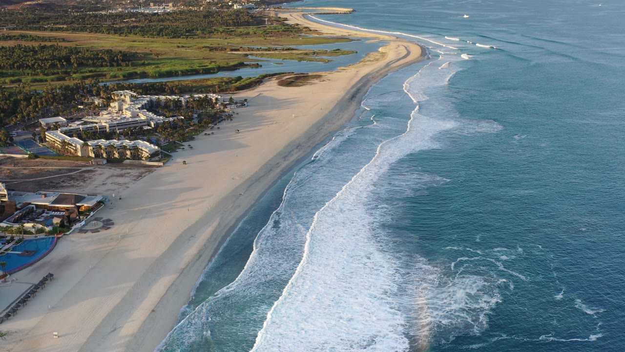 Aerial view of a sandy coastline with surf and resort buildings.