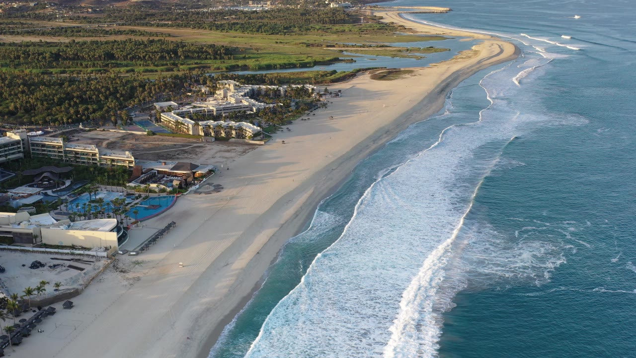 Aerial view of a sandy beach with surf breaking beside resort buildings.