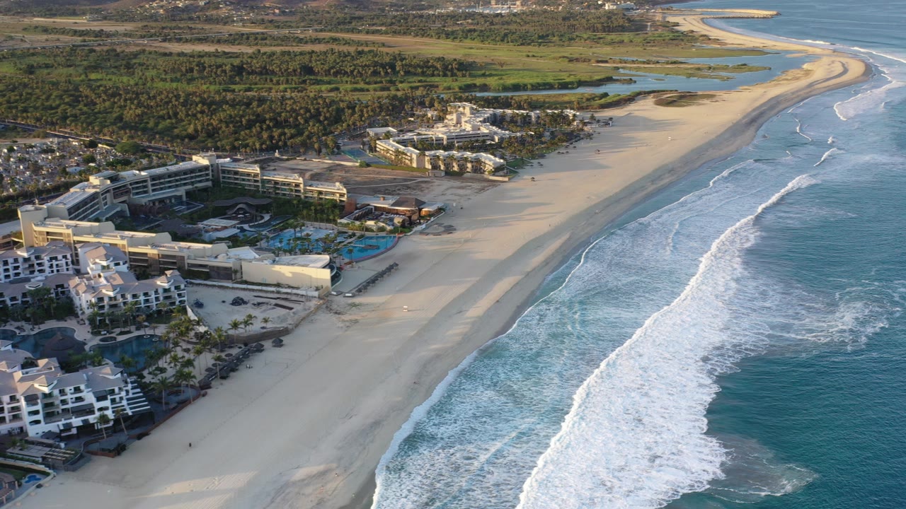 Aerial view of resort buildings beside a wide beach and breaking waves.