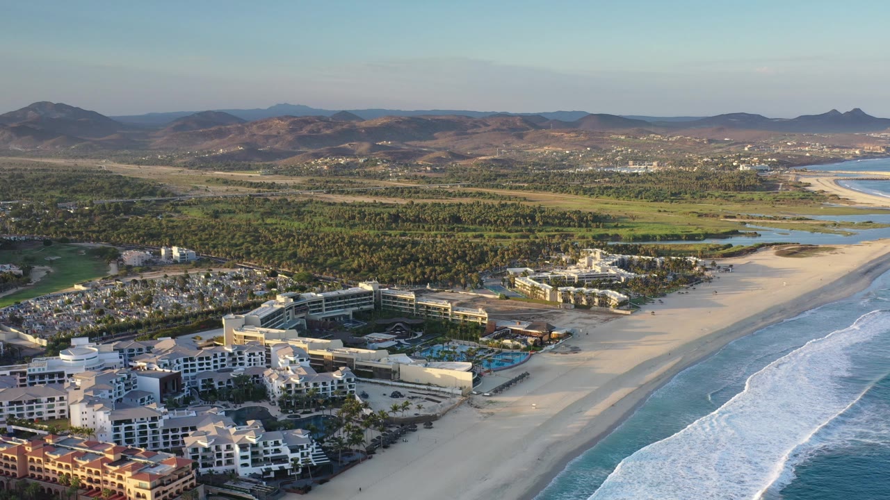 Aerial resort and coastline view with ocean waves and inland greenery.