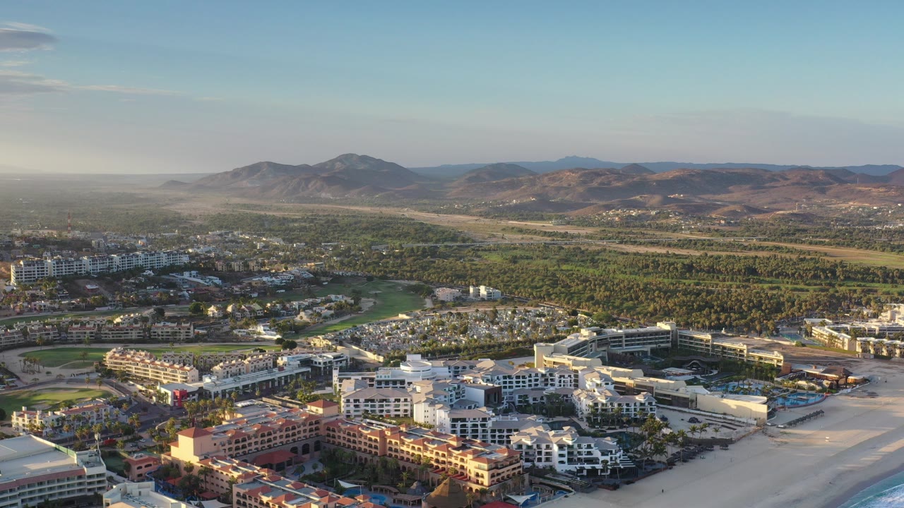 Aerial view of resort buildings, green grounds, desert hills, and blue sky.