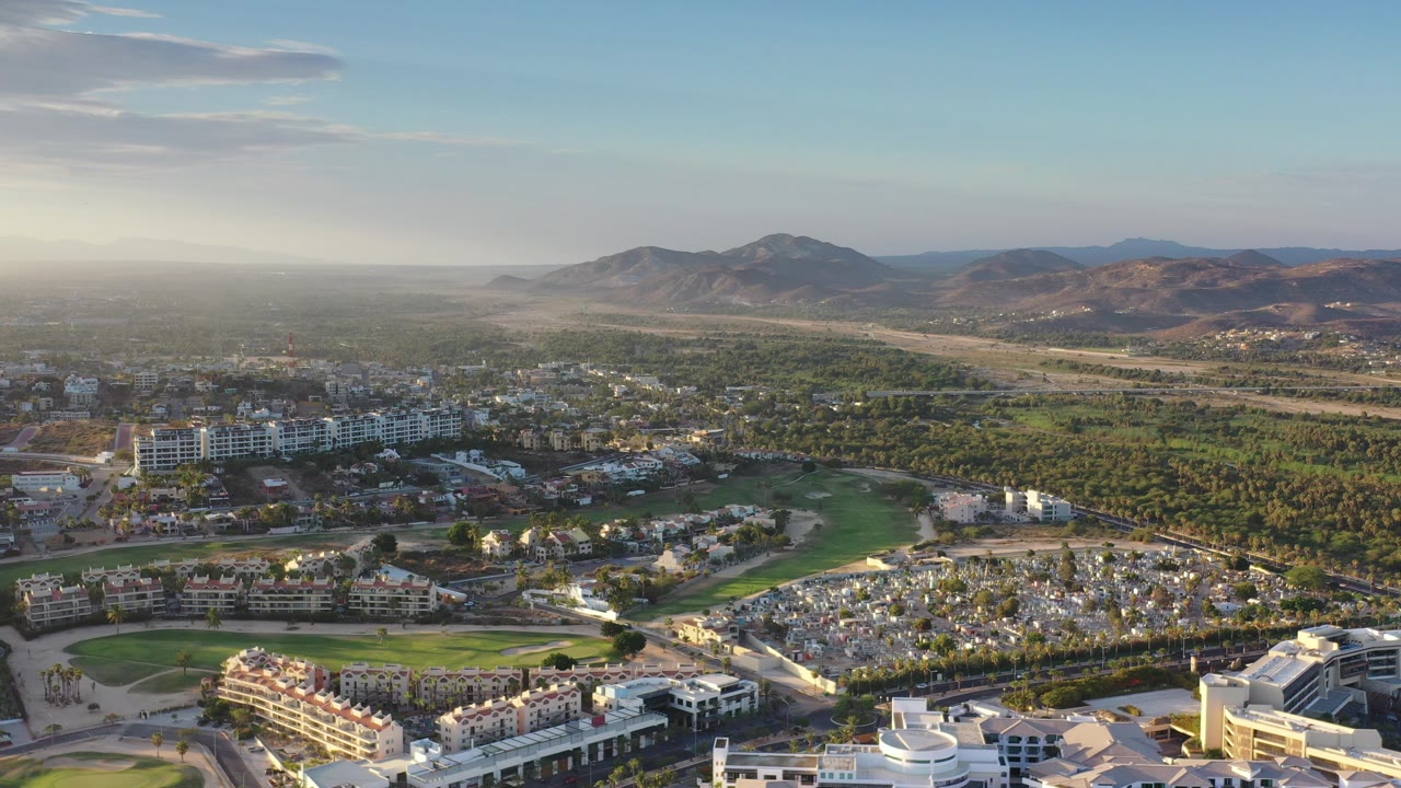 Aerial view of buildings, roads, trees, green lawns, and distant hills.