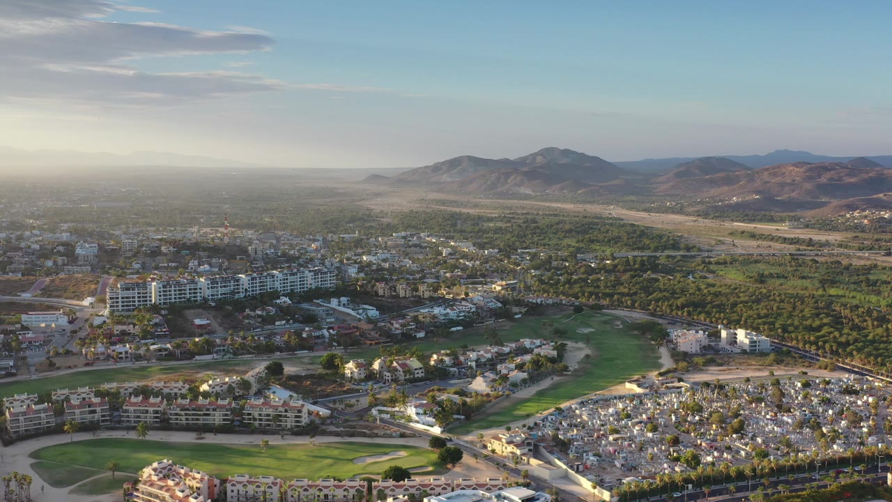 High view across resort-area buildings, golf greens, palms, and mountain ridge.