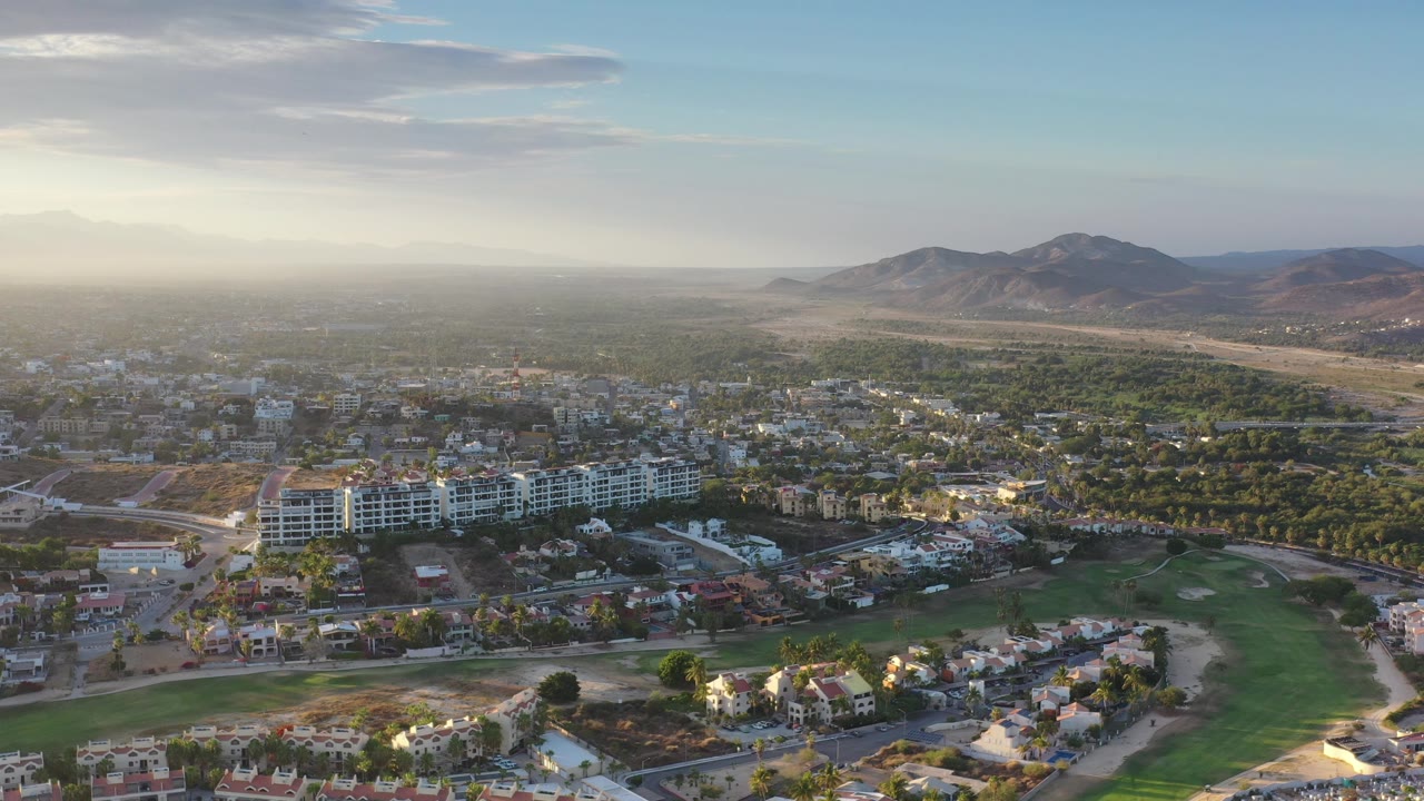 Urban edge aerial with homes, trees, open land, and mountain range