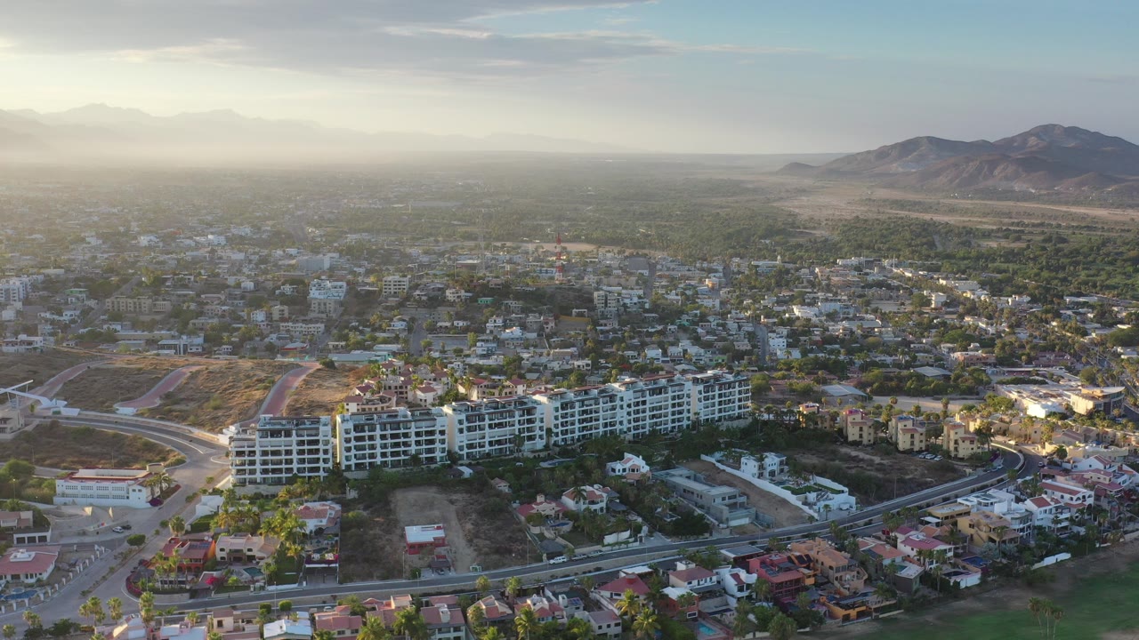 Aerial view over low-rise Los Cabos buildings with mountains in the distance.