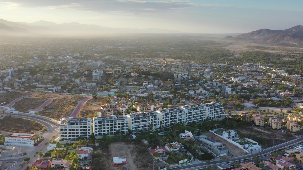 Aerial view over white mid-rise buildings, roads, city blocks, plains, and mountains.