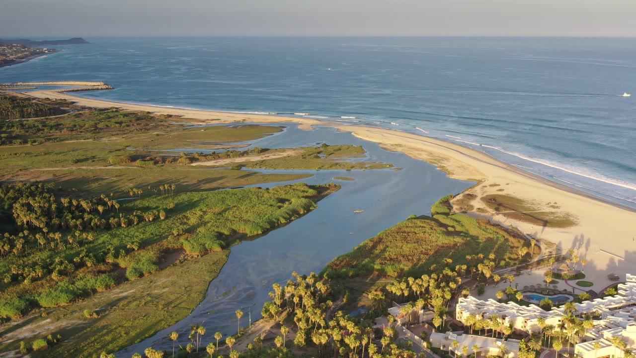 Aerial view of a river mouth, beach, marsh vegetation, and blue sea.