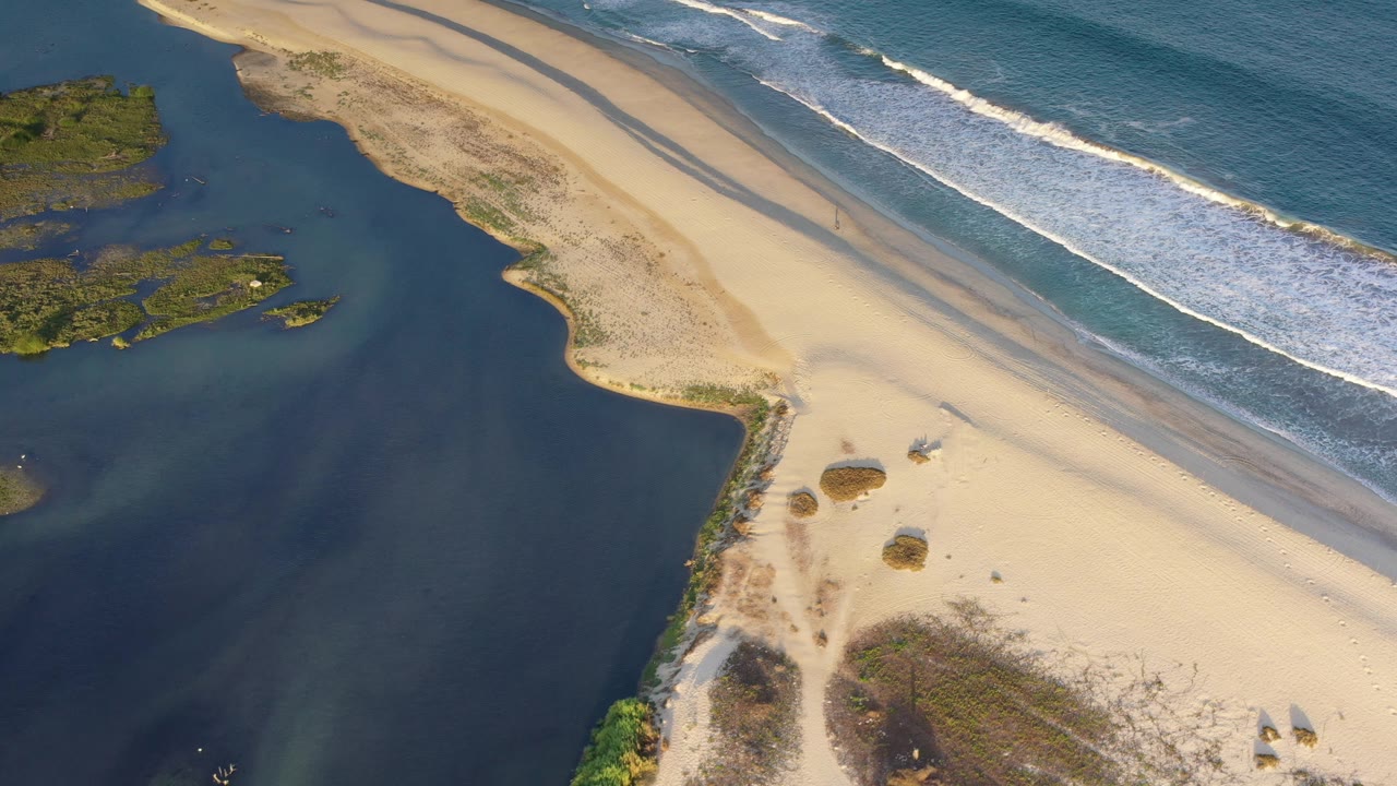 Top view of beach curve, estuary, rocks, and waves.