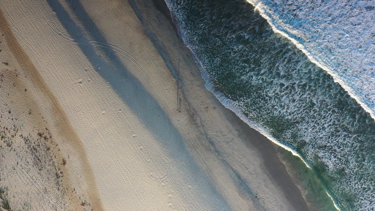 White surf approaching empty sand from above