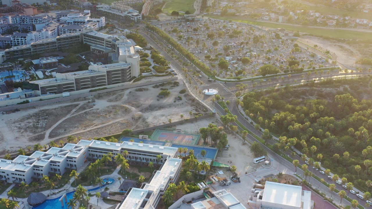 Aerial view of buildings, a curved road, tennis courts, pools, trees, and open lots.