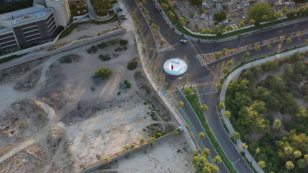 Overhead street view with a circular island, crosswalk markings, trees, and parked-looking cars.