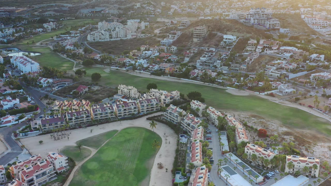 Aerial view of golf greens, homes, roads, and hillside buildings.
