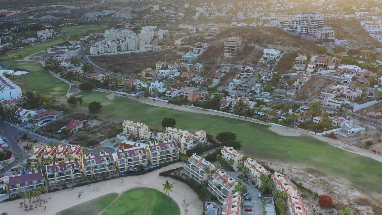 Aerial view of homes, green grass, roads, and hillside buildings at sunrise.