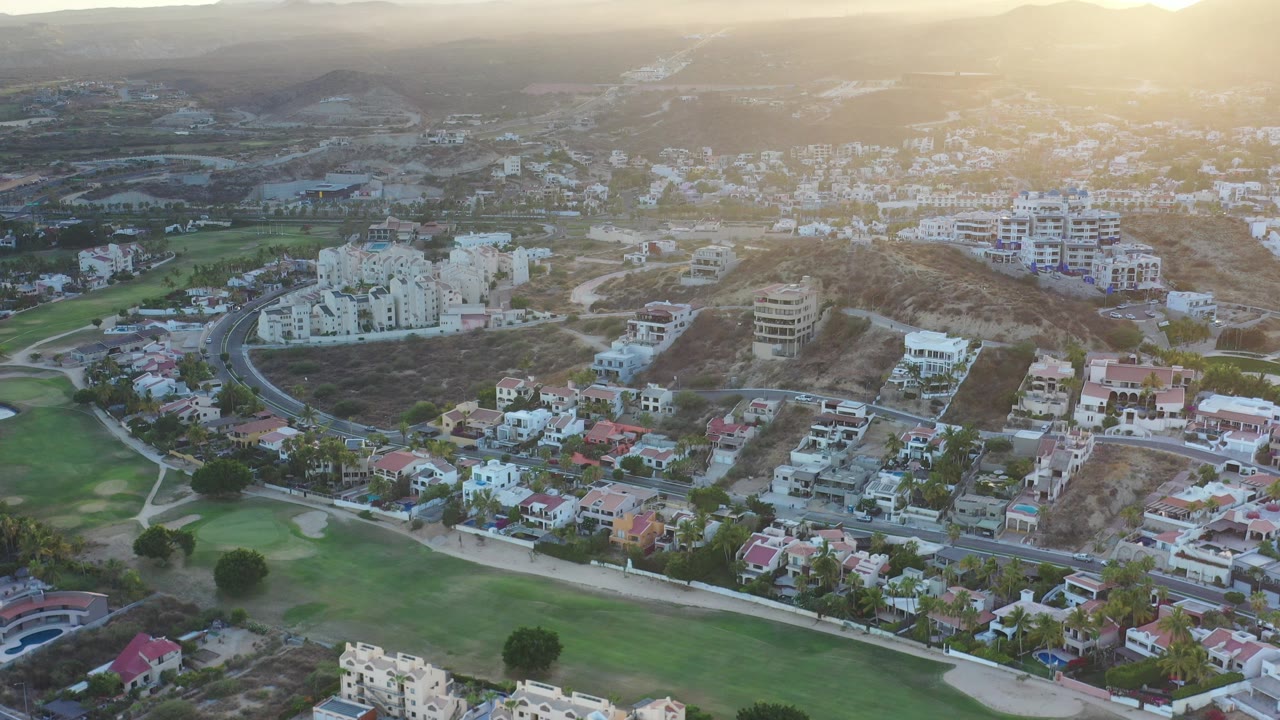 Aerial view of hillside buildings, roads, green lawns, and mountains at sunset.