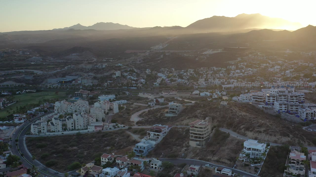 Sunset over mountains and low city buildings from a high aerial view.