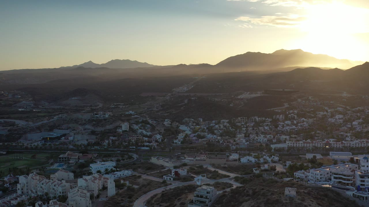 Aerial view of houses below dark hills and mountains at sunset.
