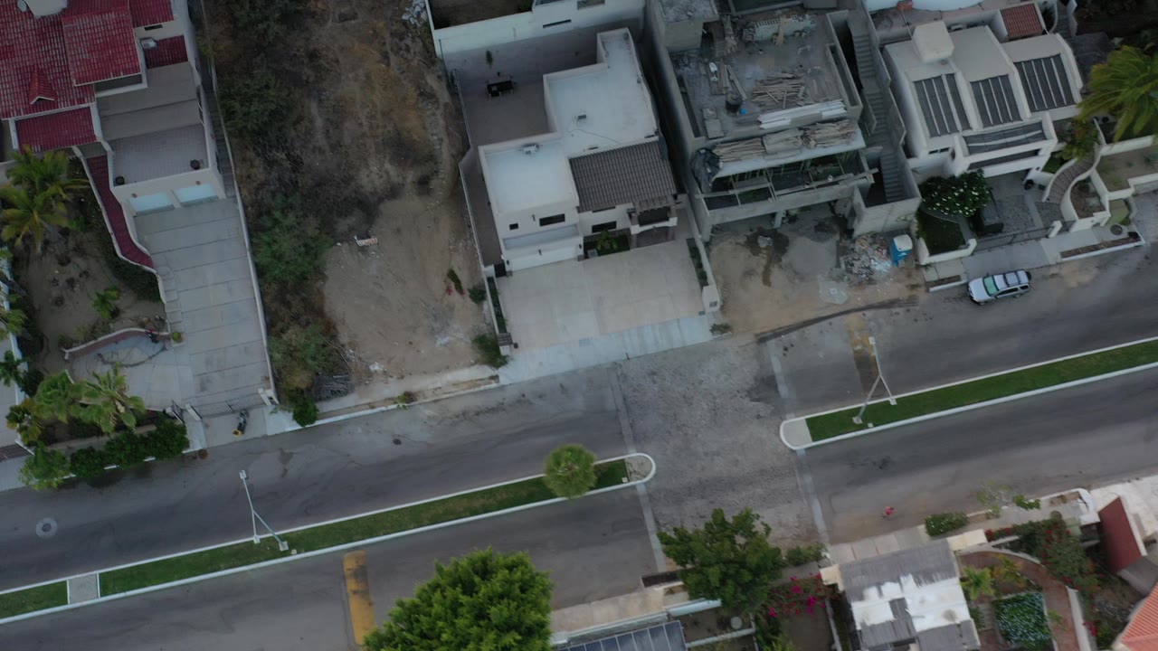 Overhead view of homes, a paved street, and an undeveloped lot.