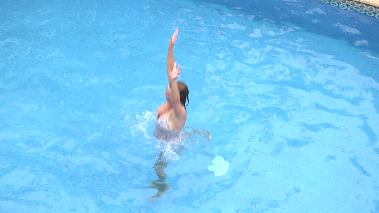 Woman in a swimsuit reaching up from blue pool water.