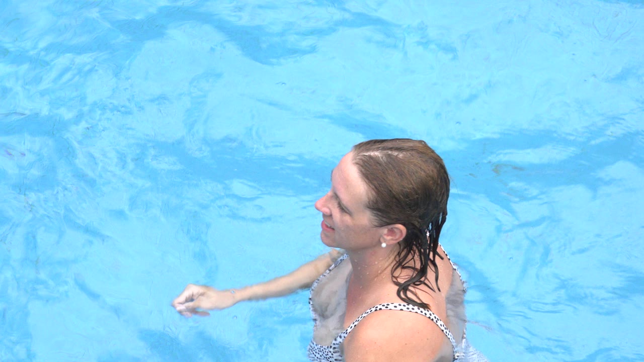 Adult woman in a patterned bikini stands chest-deep in bright blue pool water in Los Cabos, Mexico, facing left near the start of the clip.