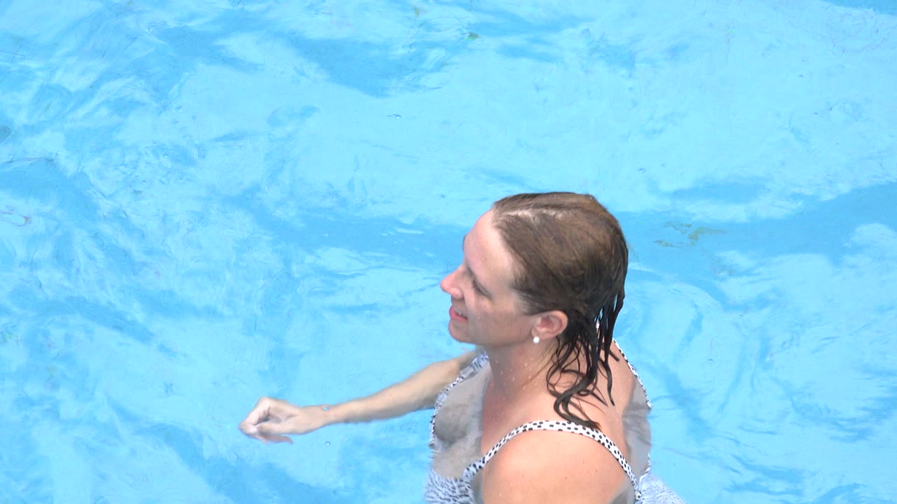 Adult woman in a patterned bikini remains chest-deep in the Los Cabos pool, with one arm bent as she moves through the blue water.